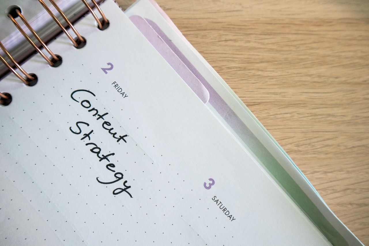 Top view of a notebook open to a day planner featuring Content Strategy handwritten, lying on a wooden desk.